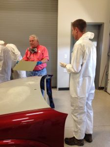 Brent Jansen standing in front of red and white car hood while listening to instructor
