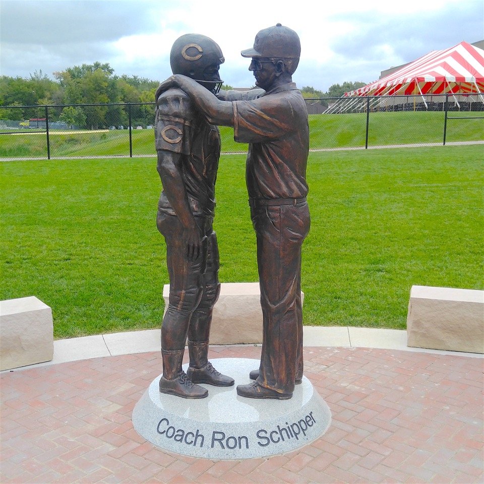 Bronze statue of football coach with hands on shoulders of football player