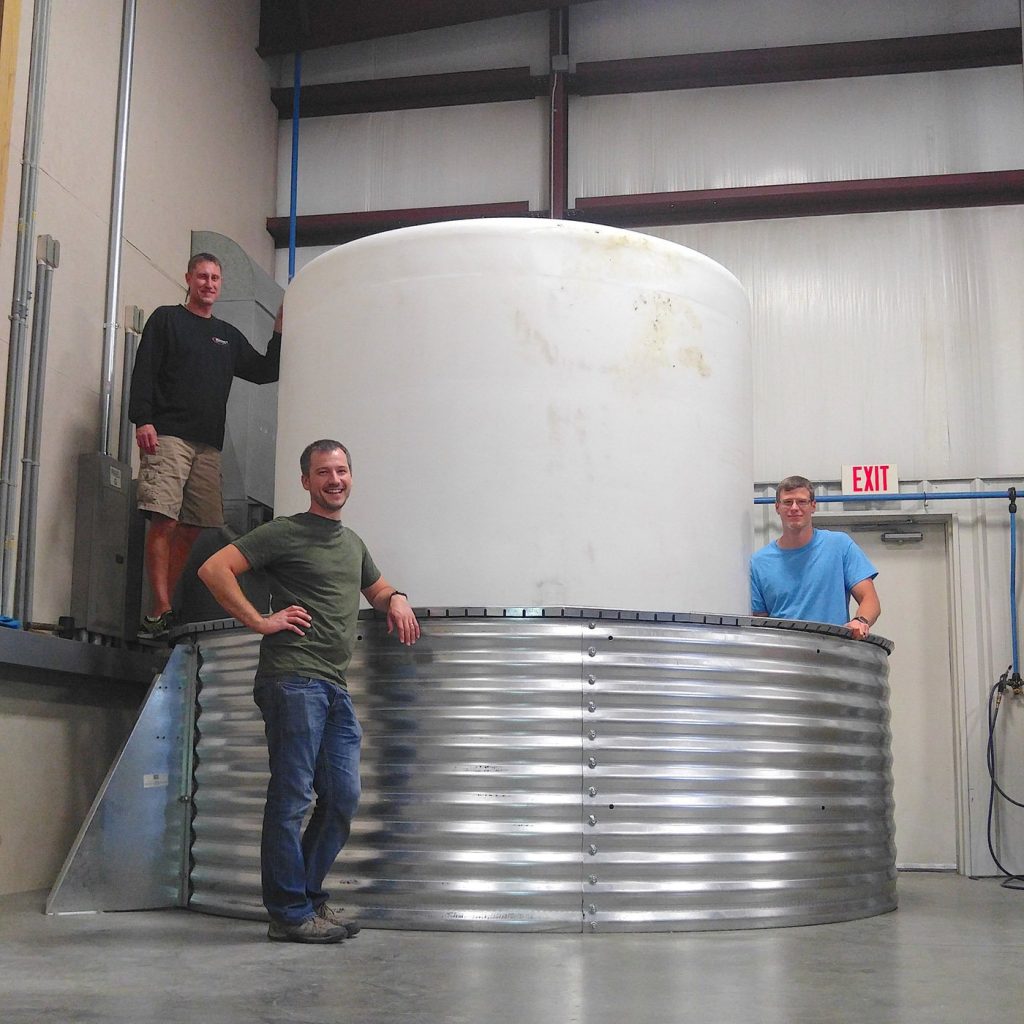 PEC team poses in front of water tank in workshop