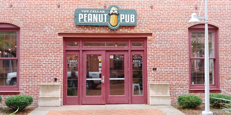 Storefront sign with peanut logo with mustache and glasses mounted on brick wall above door