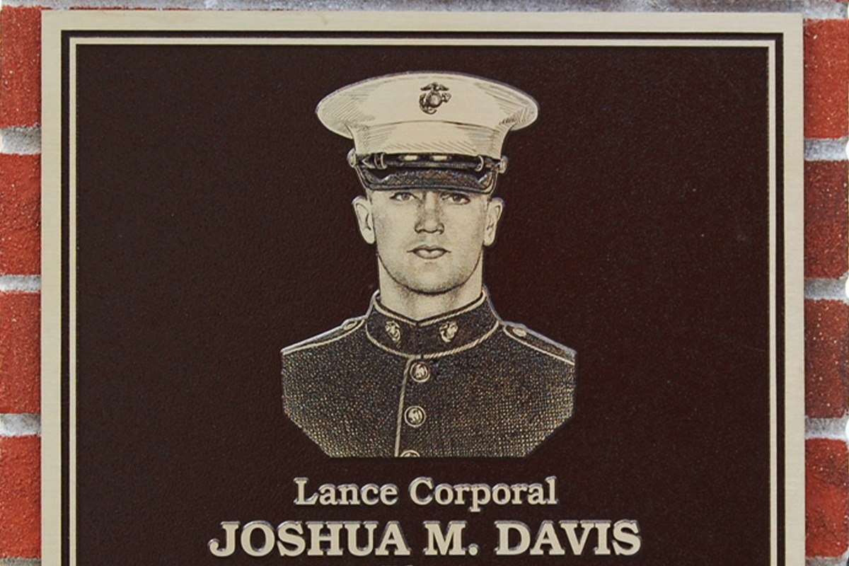 Black and gold Lance Corporal Joshua M. Davis zinc memorial plaque on brick wall