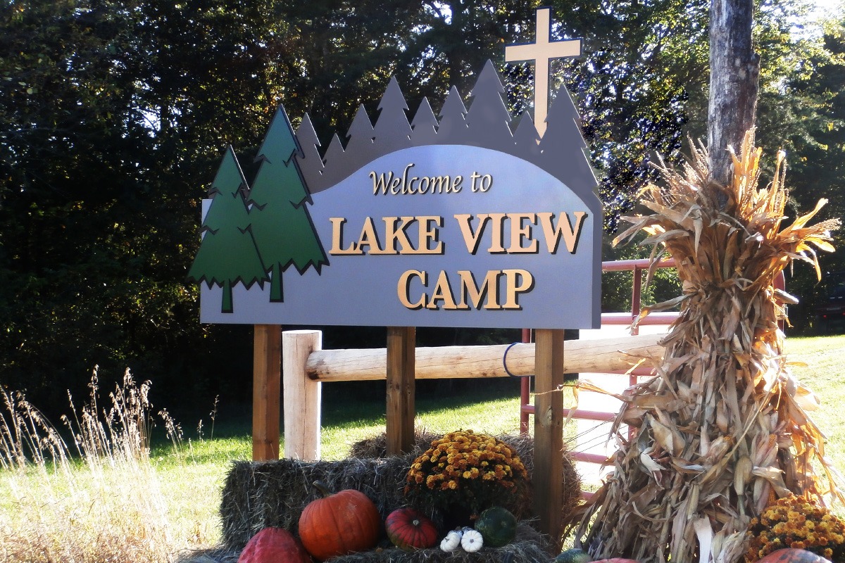Post-and-panel Lave View Camp sign with evergreen trees and cross