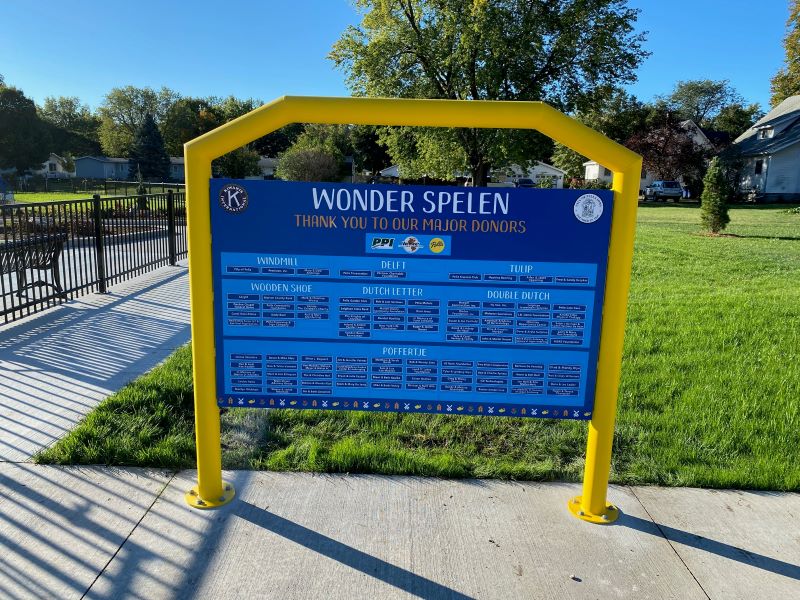 Yellow and blue Wonder Spelen donor wall with green grass and blue sky